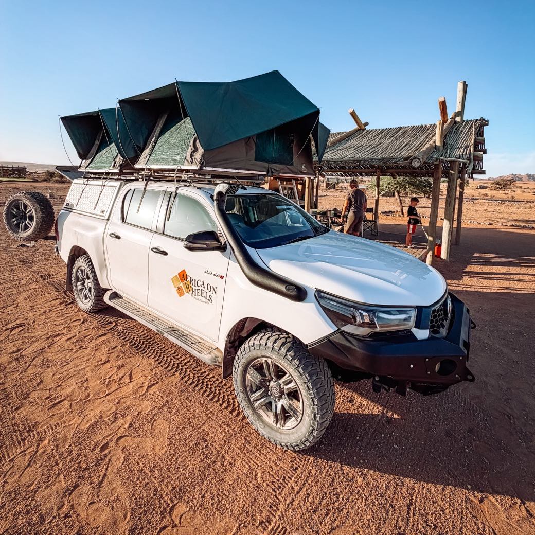 Bílé expediční auto 4×4 se dvěma rozloženými střešními stany v kempu na červeném písku