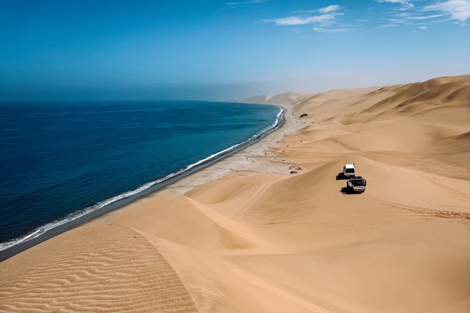 Dvě auta 4×4 na hřebeni duny nad oceánem v Sandwich Harbour
